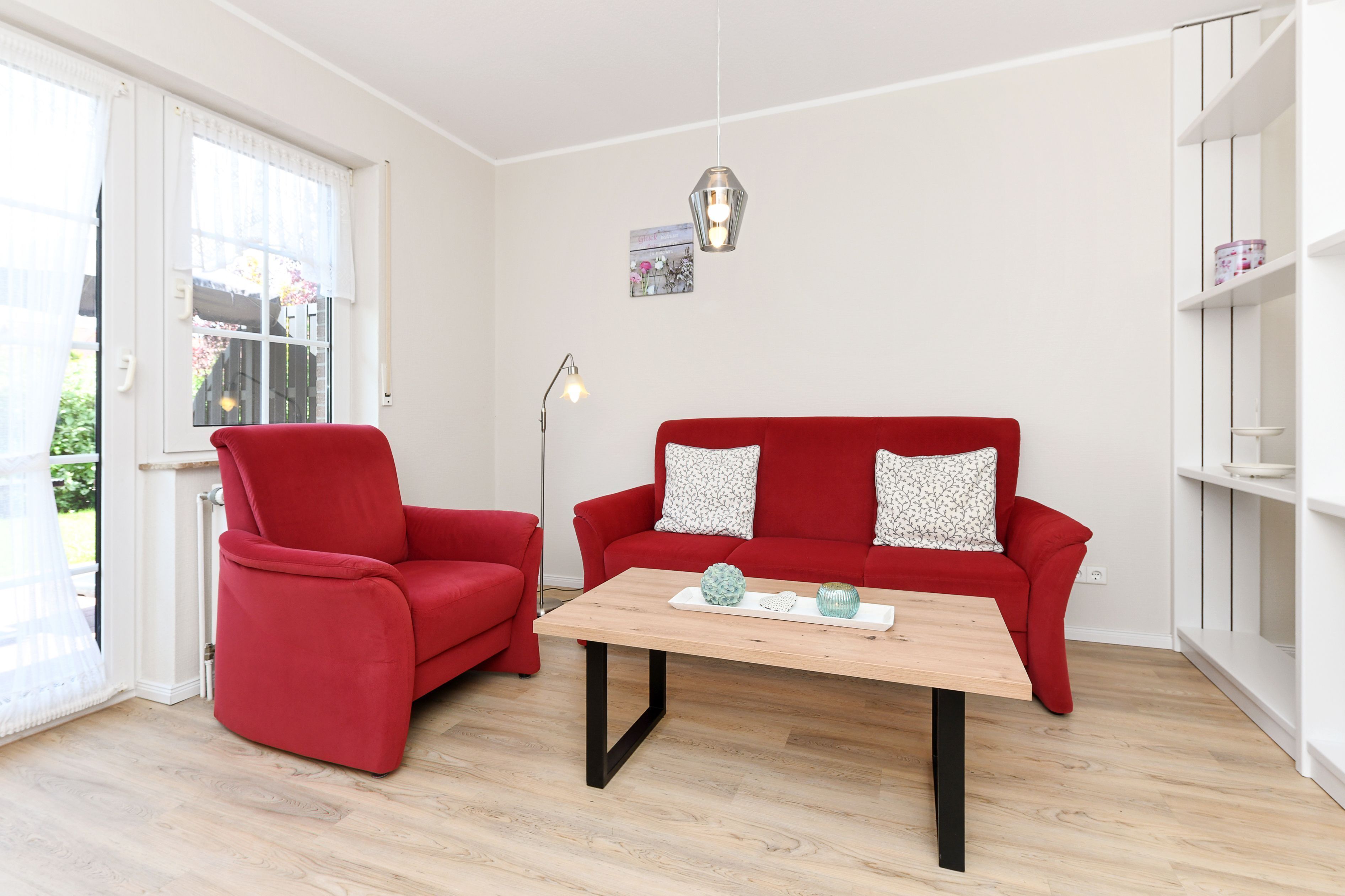 A modern living room with a red sofa, a matching armchair, a wooden coffee table, and a pendant light.