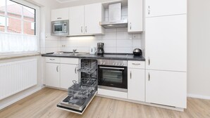 A modern kitchen with white cabinets, a built-in oven, a microwave, and a dishwasher. - Sandpiper - Haus Andreesen (Neuharlingersiel)