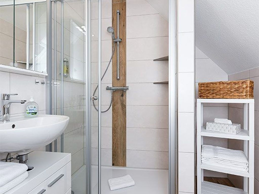 Un baño moderno con cabina de ducha de vidrio, un lavamanos blanco y un estante de madera con toallas.