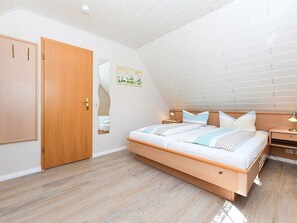 Une chambre à coucher avec un lit en bois, une table de chevet, une étagère fixée au mur et une porte.
