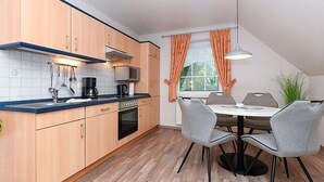 A modern kitchen with wooden cabinets, a built-in oven, and a dining area with a table and chairs.