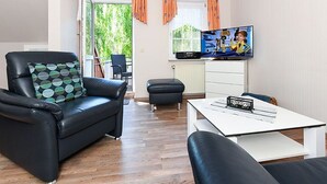 A modern living room with a black leather sofa, a white coffee table, and a television on the wall.