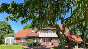 A large brick house with a red-tiled roof, a covered porch, and a well-maintained garden.