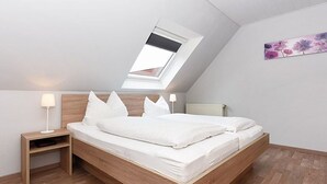 A modern bedroom with a sloped ceiling, a skylight, a wooden bed frame, and a nightstand with a lamp.