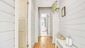 Un pasillo con paredes de madera blanca y suelo de madera. Hay un banco con objetos decorativos.