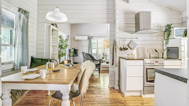 Una cocina con pisos de madera, armarios blancos, una estufa y un comedor con mesa y sillas.
