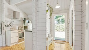 Una cocina con armarios blancos, microondas y estufa. El suelo es de madera y se ve follaje a través de la ventana.