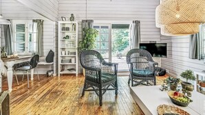 Un salón espacioso con piso de madera, dos sillones de mimbre, una mesa de centro blanca y una estantería llena de libros y objetos decorativos.