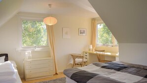 Una camera da letto con un letto, una scrivania e una sedia. Sono presenti due finestre e una lampada a soffitto.