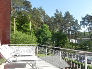 Een balkon met een witte metalen hekwerk, een witte fauteuil met kussen en een potplant.