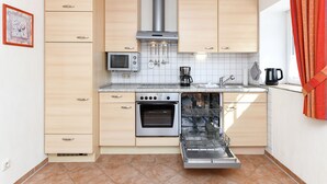 A compact kitchen with light wooden cabinets, a stainless steel oven, a microwave, and a dishwasher. - Vacation apartment Strandkrabbe - Haus an der Burg (Werdum)