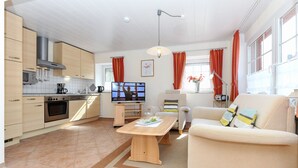 A modern kitchen with built-in appliances, a dining area with a table and chairs, and a living room with a sofa and a TV. - Vacation apartment Strandkrabbe - Haus an der Burg (Werdum)
