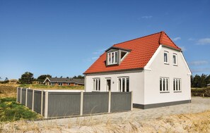 Set amidst a serene beachside landscape, this charming home features a gabled facade with a dormer window and a red-tiled roof.