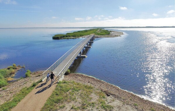 Cross a serene waterway via a sturdy metal-railed bridge, surrounded by lush grassy banks and a dirt path.