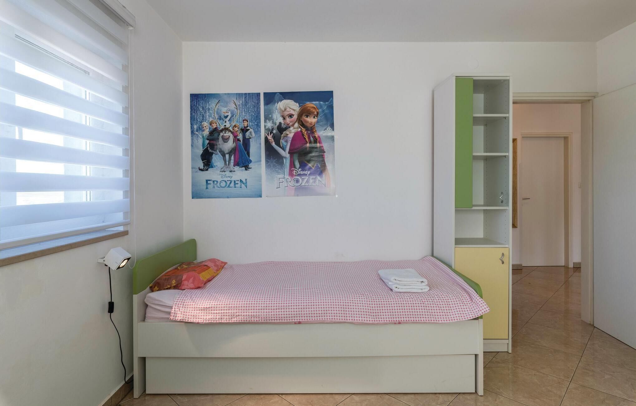 Ein Schlafzimmer mit einem Bett, einem Nachttisch, einer grünen Regaleinheit und zwei Postern an der Wand.