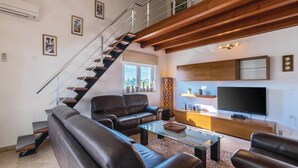 Een moderne woonkamer met een trap, leren banken, een glazen salontafel, een flatscreen televisie en een decoratief kunstwerk aan de muur.