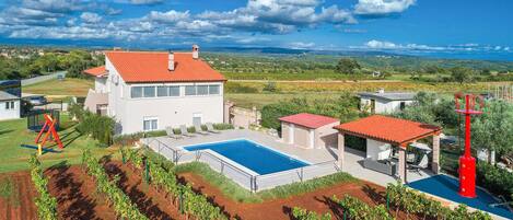 A large house with a swimming pool, vineyard, and red-roofed structures.