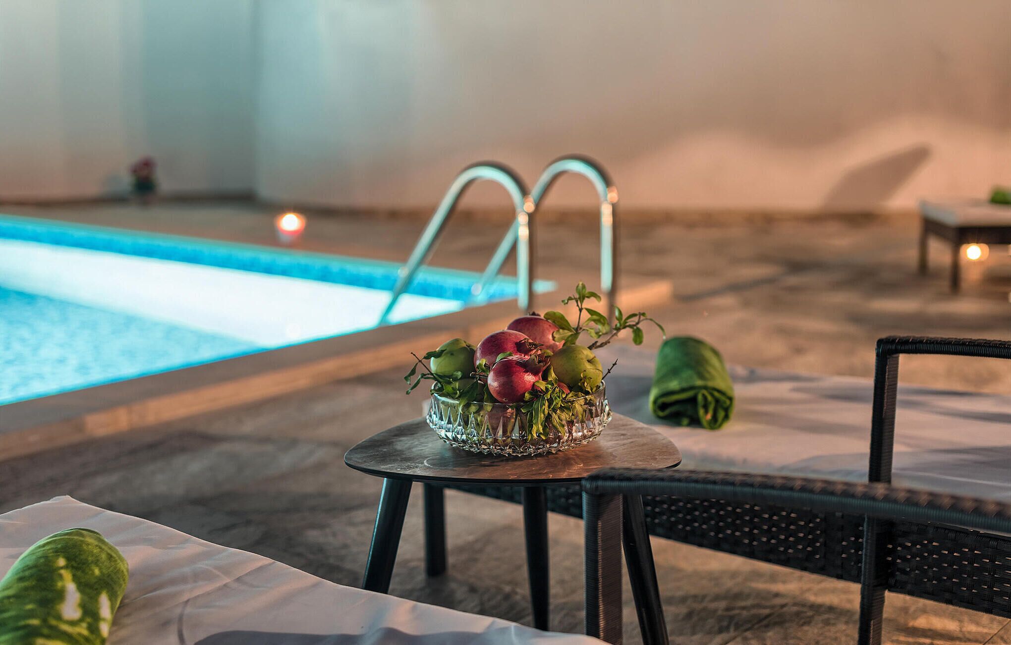 Zona de piscina amb taula de vidre que sosté un plat de fruita, una cadira i una taula petita amb una espelma.