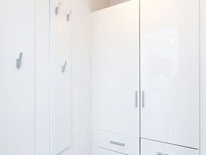 Une armoire blanche à deux portes et un tiroir, avec des poignées argentées et une petite étagère en haut.