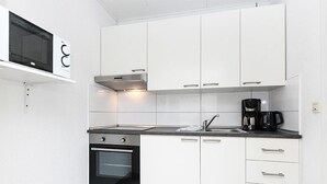 Una cocina moderna con armarios blancos, horno empotrado, microondas y cafetera.