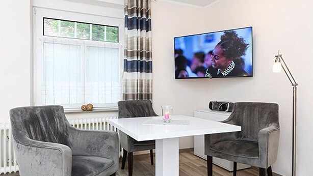 Una sala de estar moderna con una mesa blanca, sillones grises, un televisor de pantalla plana y una lámpara de pie.