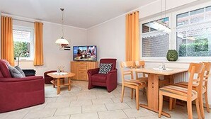 A living room with a sofa, armchair, dining table, chairs, and a TV. - Apartment New Guesthouse - Haus an der Burg (Werdum)