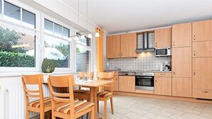A kitchen with wooden cabinets, a dining table with chairs, and a window with a view of greenery outside. - Apartment New Guesthouse - Haus an der Burg (Werdum)