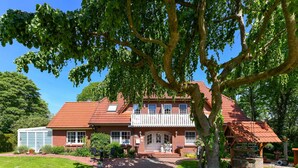 A large brick house with a red-tiled roof, a covered porch, and a well-maintained garden. - Apartment New Guesthouse - Haus an der Burg (Werdum)
