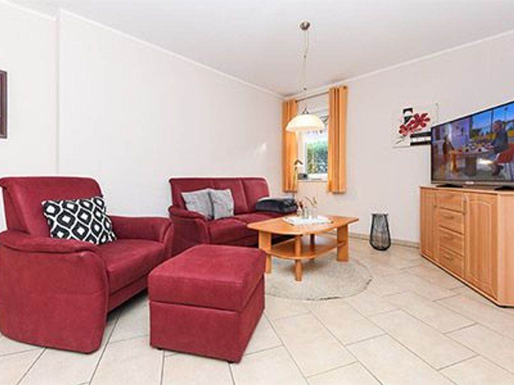 Ein modernes Wohnzimmer mit einem roten Sofagarnitur, einem Holztisch und einem Fernseher auf einer Holzkommode.