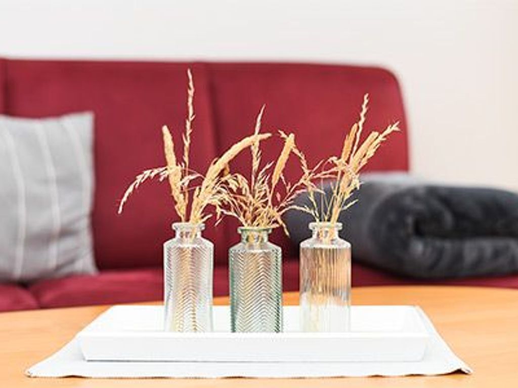 Een witte dienblad met vier glazen vazen gevuld met gedroogde planten op een houten tafel.