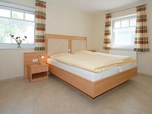 Une chambre à coucher avec un lit en bois, une table de chevet, une lampe et une fenêtre avec des rideaux.