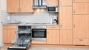 A kitchen with wooden cabinets, a microwave, a dishwasher, and an oven. - Apartment New Guesthouse - Haus an der Burg (Werdum)