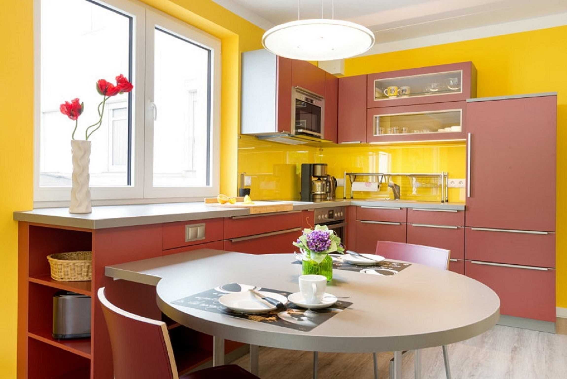 Una cucina moderna con pensili gialli e rossi, un tavolo rotondo e una finestra con fiori rossi.