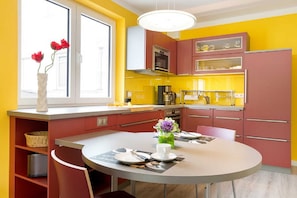A modern kitchen with yellow and red cabinets, a round dining table, and a window with red flowers.