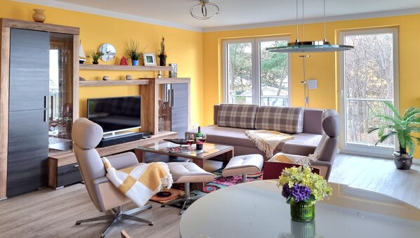 A modern living room with a sofa, armchairs, a TV, and a dining table.