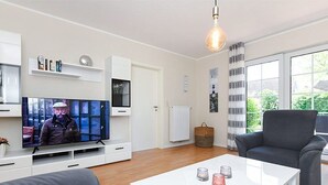 Ett modernt vardagsrum med en platt-TV, ett vitt soffbord, en grå soffa och en grå fåtölj.