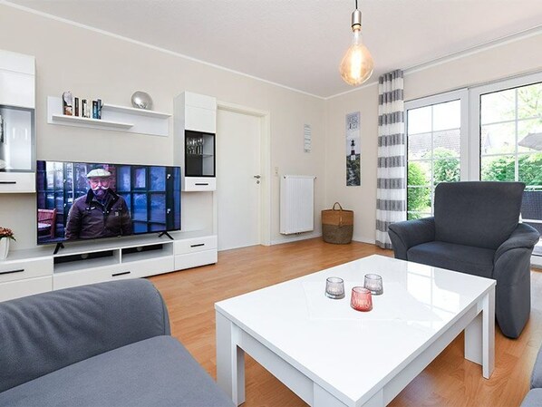 Un salon moderne avec un téléviseur à écran plat, une table basse blanche, un canapé gris et un fauteuil gris.