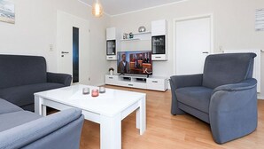 Ett modernt vardagsrum med ett vitt soffbord, två grå soffor, en grå fåtölj och en tv som står på en vit tv-bänk.