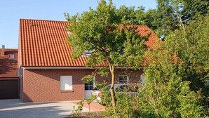 Een tweelaags bakstenen gebouw met een dak van rode tegels, een garage die zichtbaar is en een kleine boom op de voorgrond.