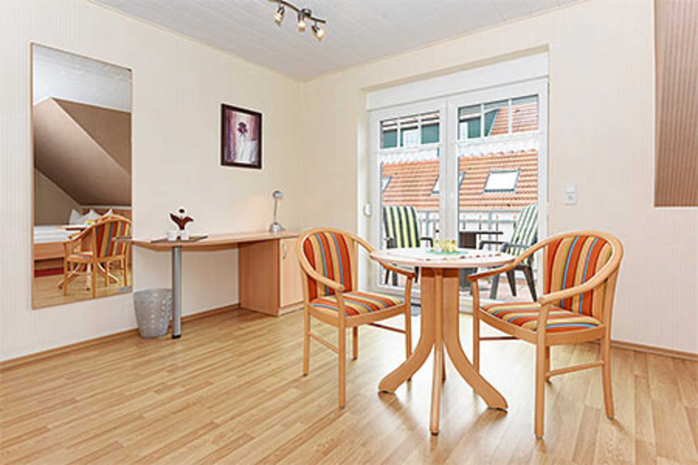 A room with a wooden floor, a round table with chairs, a desk, and a large mirror.