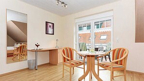 Een kamer met een houten vloer, een ronde tafel met stoelen, een bureau en een grote spiegel.