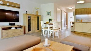 Un salon moderne doté d’un téléviseur à écran plat, de meubles en bois, d’un coin repas et d’une cuisine.