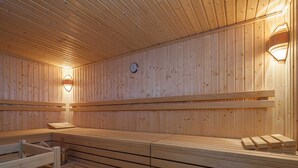Un sauna avec des bancs et des murs en bois, une horloge et des lampes fixées au mur.