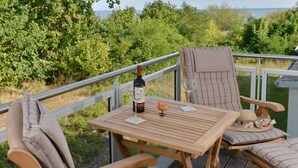 Une terrasse en bois avec une table et des chaises, une bouteille de vin et un verre posé sur la table.