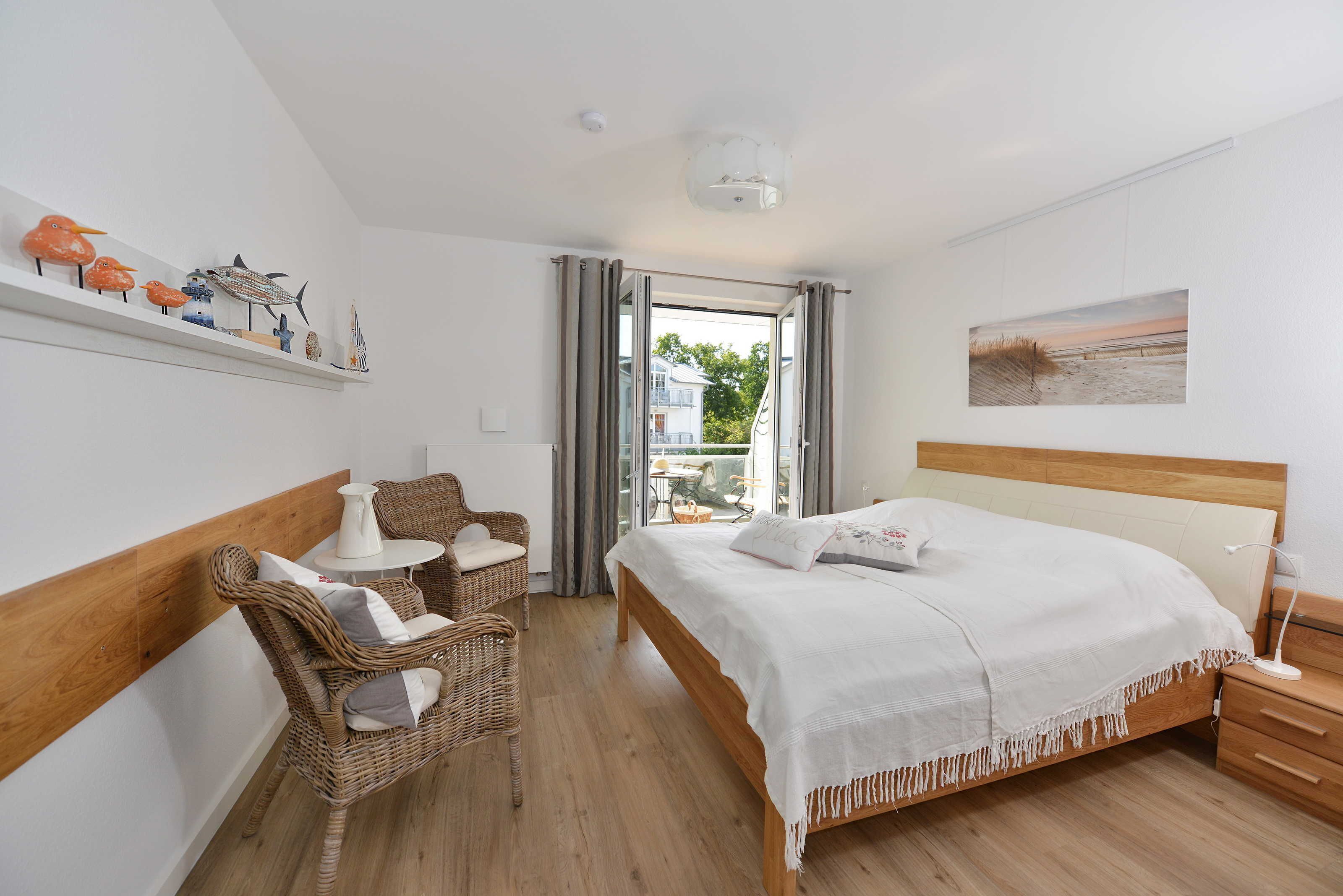 A bedroom with a bed, a chair, a small table, and a shelf with decorative items.