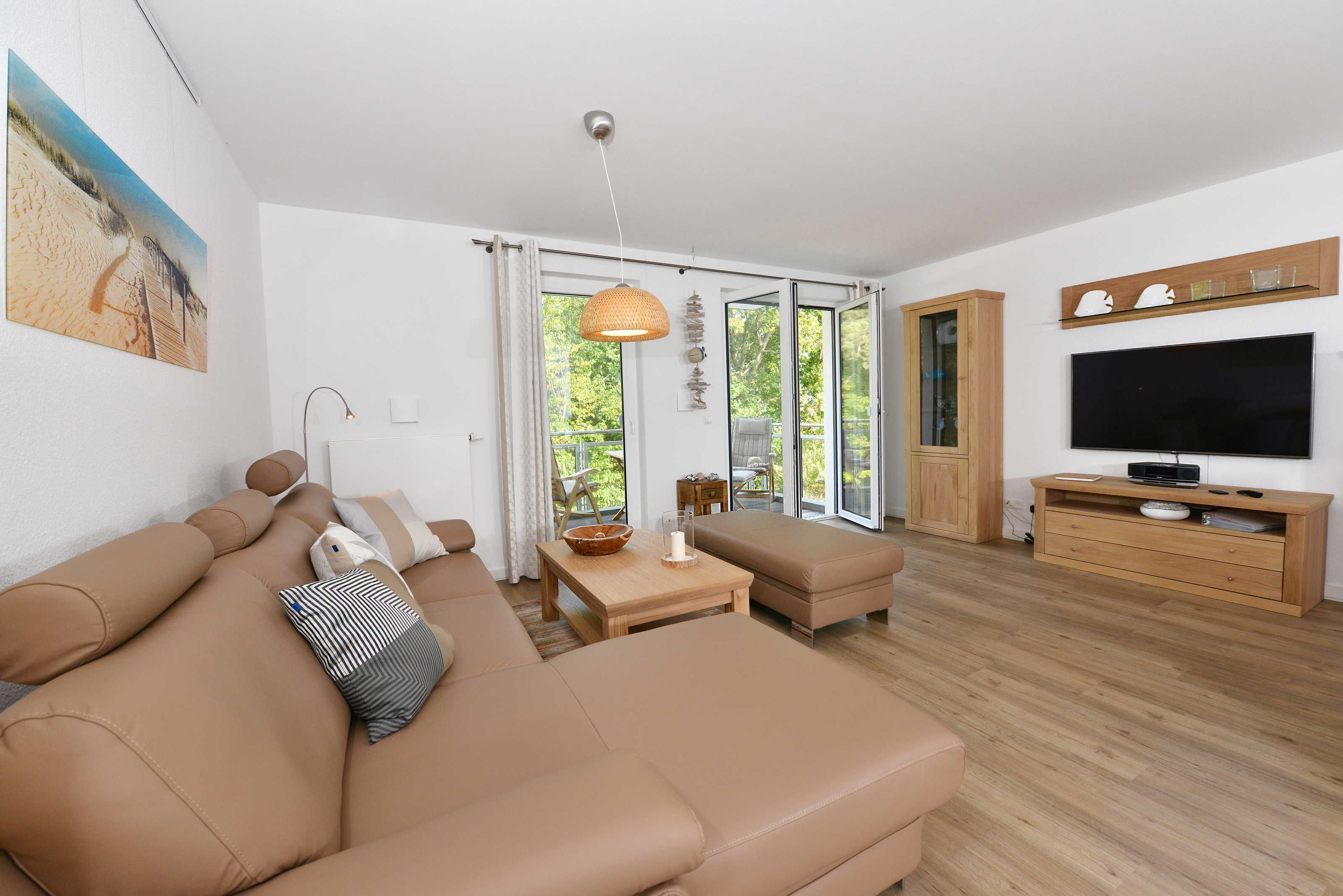 A modern living room with a beige sofa, a wooden coffee table, and a television on a wooden stand.