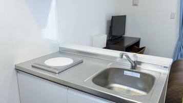 A modern kitchen with a stainless steel sink, a digital scale, and a flat-screen TV in the background.