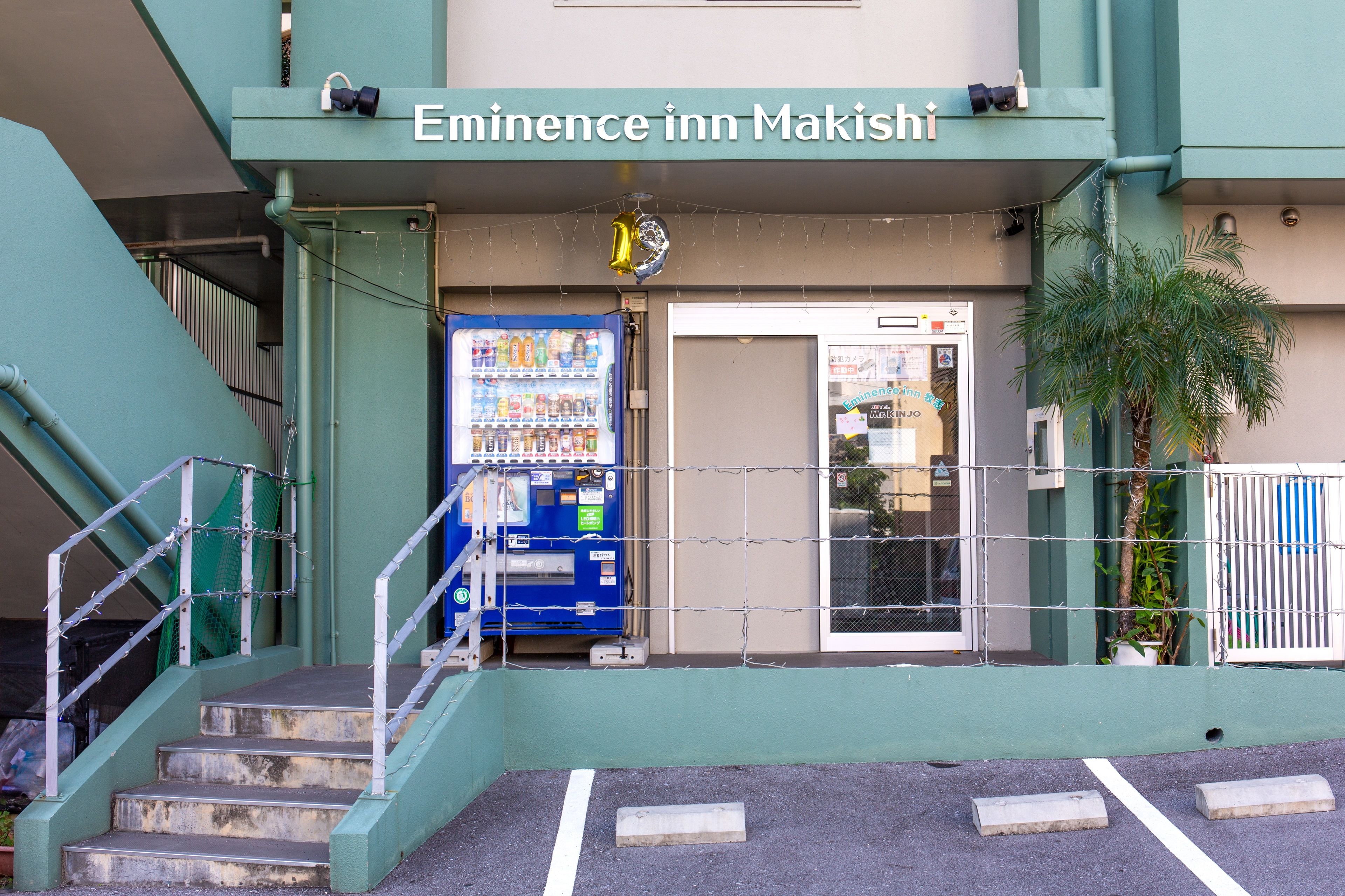 Exterior del Emina Inn Makishi, con una máquina expendedora, una escalera y una entrada protegida por barrotes.