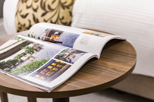 An open magazine on a round wooden table with a cushion in the background. - Mr.KINJO EMINENCE INN MAKISHI (Naha)