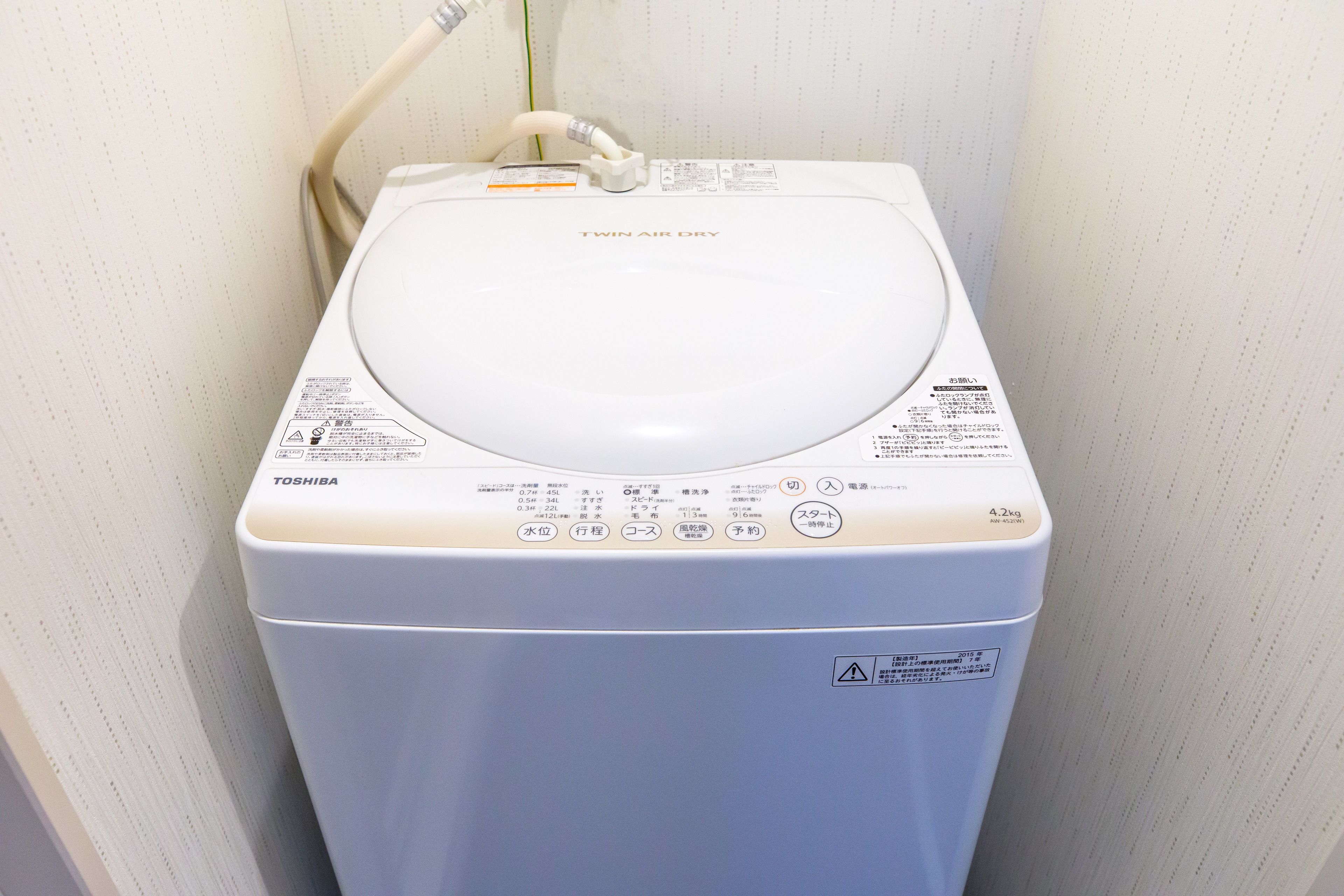 A white Toshiba Twin Air Dry washing machine with a control panel and a hose.